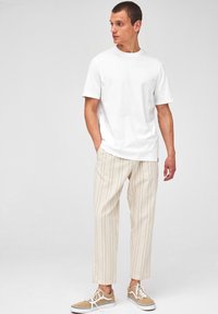 T-shirt blanc à manches courtes, coupe décontractée, associé à un pantalon à rayures de couleur claire et des baskets beige avec des lacets blancs.