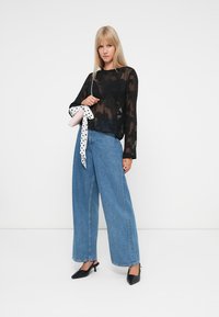 Sort gennemsigtig langærmet top med blomsterprint, parret med højtrådige lyseblå bredbenede jeans og sorte spidsede hæle.