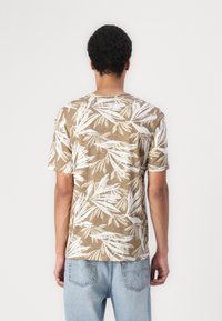 Kortærmet, olivengrøn t-shirt med hvidt tropisk bladmønster, rund hals og afslappet pasform, parret med lyseblå denimjeans.