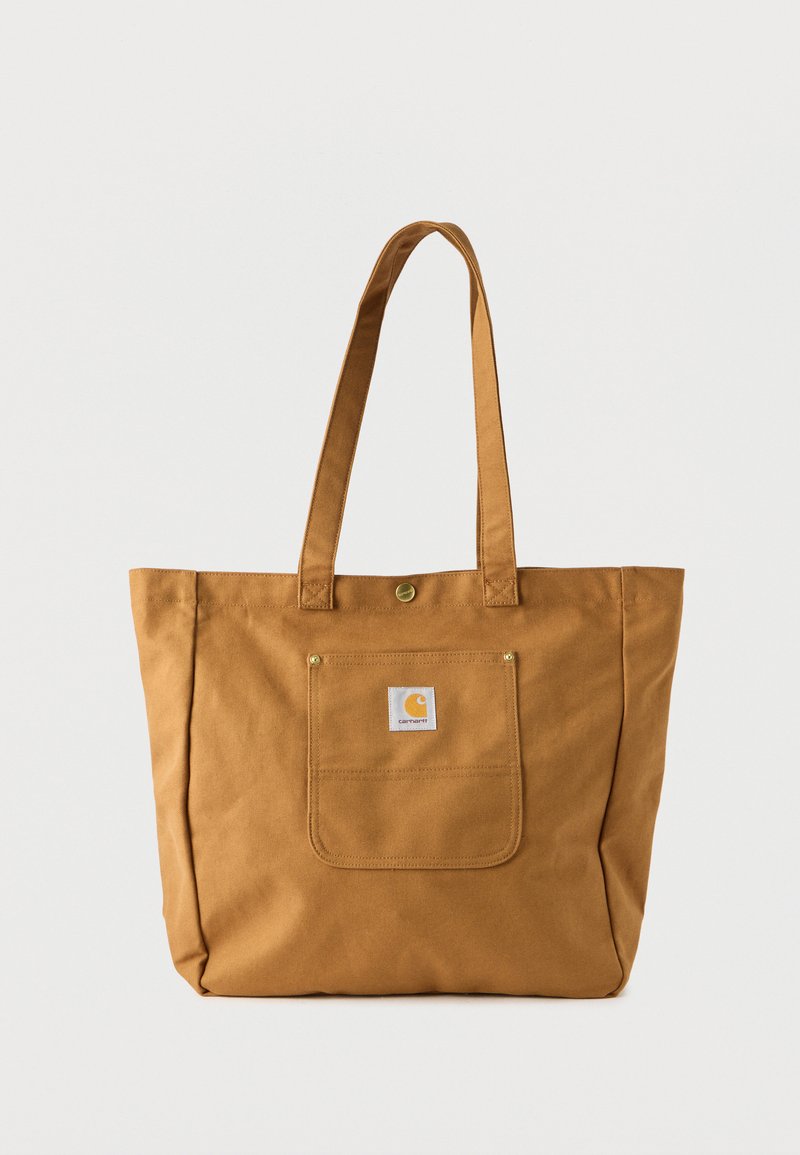 Καφέ τσάντα tote Carhartt με μακριές λαβές, μπροστινή θήκη και μικρή λογότυπο κονκάρδα, τοποθετημένη σε απλό λευκό φόντο.