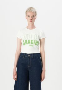 Hvit kortermet t-skjorte med grønn grafisk tekst "RIO DE JANEIRO" og "1995", kombinert med høy midje mørke denimbukser.