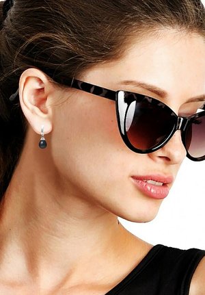 Lunettes de soleil en forme de chat avec un motif écaille de tortue foncé, verres dégradés. Boucles d'oreilles pendantes en argent avec un détail en forme de goutte noire. Haut noir.