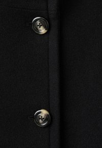 Abrigo de lana negra con textura suave, costuras detalladas y dos botones brillantes con diseño de cuatro orificios.