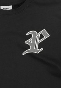 Czarna koszulka wykonana z bawełny z wypukłym srebrnym logo po lewej stronie klatki piersiowej, z unikalnym, stylizowanym wzorem. Gładka tekstura.