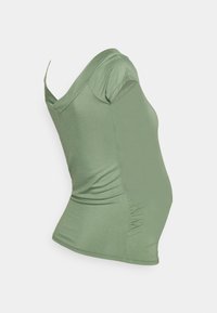 Top de maternidade verde claro com mangas curtas, decote em forma de U e detalhes franzidos nas laterais para acomodar uma barriga em crescimento.