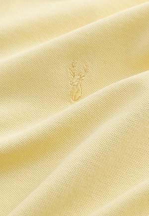 Svijetložuta tkanina sa teksturiranim tkanjem, s diskretnim izvezenim logotipom jelena vidljivim u materijalu. Meka i glatka tekstura.