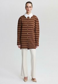 Bruine en beige gestreepte overhemd met knoopsluiting, een witte kraag, lange mouwen en een ontspannen pasvorm. Gecombineerd met crèmekleurige uitlopende broeken en beige hakken.