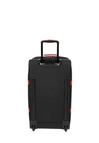 Maleta negra con ruedas, con un mango retráctil, acentos rojos, material resistente y textura suave; diseñada para ser duradera y facilitar el transporte.