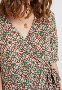Kwiatowa sukienka w kratkę z brązowym tłem i różowymi oraz niebieskimi kwiatami, z dekoltem w kształcie litery V oraz detalem w postaci wiązania z boku. Krótkie rękawy w zestawie.