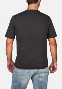 Schwarzes kurzärmliges T-Shirt aus Jersey-Stoff, mit Rundhalsausschnitt und glatter Textur, getragen zu hellblauen Jeans.