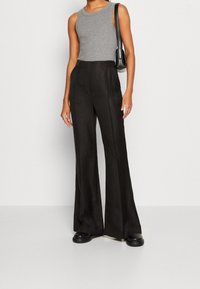 Szary top bez rękawów w połączeniu z wysokim stanem i luźnymi czarnymi spodniami. Spodnie mają subtelną fakturę i szerokie nogawki. Czarna torebka na ramieniu.