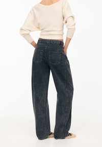 Tummanharmaat leveälahkeiset farkut, joissa on haalistunut pinta, kahdella takataskulla ja korkealla vyötäröllä. Yhdistetty vaaleankermanväriseen neulepaitaan.