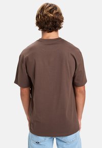 Brun bomulds T-shirt med rund halsudskæring og korte ærmer, der viser ren syning og en afslappet pasform set bagfra.