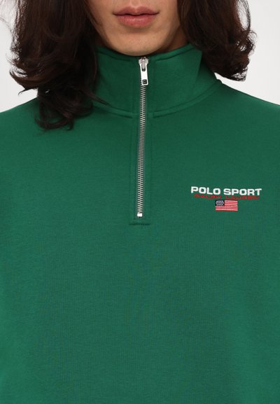 Grønn zip-up hettejakke laget av et mykt stoff, med høy krage, brodert "POLO SPORT"-logo og amerikansk flaggdetalj.
