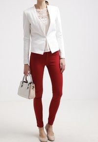 Blazer bianco strutturato, top in pizzo, pantaloni rossi aderenti, borsa beige e décolleté nude. Design semplice con linee pulite e colori a contrasto.