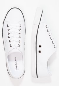 Weiße Leinenschuhe mit schwarzen Akzentstreifen, rundem Zehenbereich und sechs Metallösen. Verfügen über eine strukturierte Sohle und ein auf die Innensohle gedrucktes Logo.