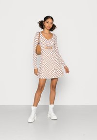 Vestido de manga longa em padrão de xadrez castanho e branco, com detalhe de laço na frente e saia rodada, combinado com botas de combate brancas.