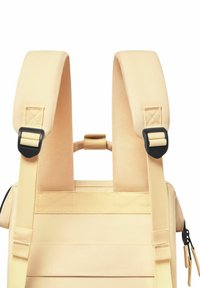 Beige backpack with thick padded straps. Features black plastic buckles and a top handle. Textured material with horizontal stitching accents.