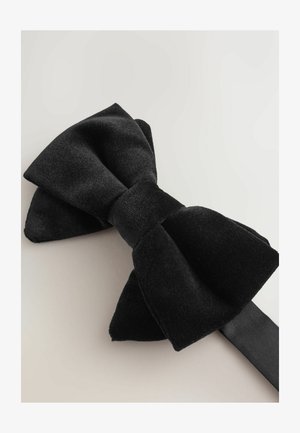 Czarny aksamitny muszka o gładkim wykończeniu, z centralnym węzłem i dwoma szerokimi, zaokrąglonymi końcami. Dołączona jedwabna wstążka do zapięcia.