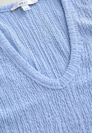 Svetle modrý pletený top s výstřihem do V, textura a žebrované okraje, vhodný pro volnočasové nošení. Viditelná značka.