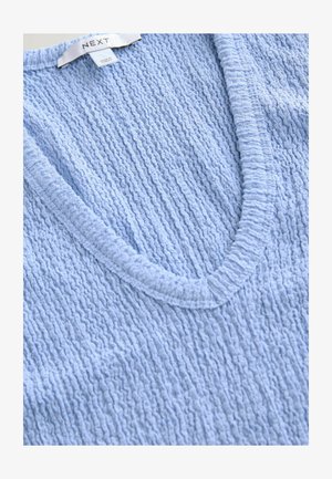 Svetle modrý pletený top s výstřihem do V, textura a žebrované okraje, vhodný pro volnočasové nošení. Viditelná značka.