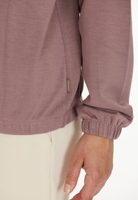 Licht mauve langemouw top met een geplooide manchet, zijnaaddetail en een klein merketiketje nabij de zoom. Zachte, gestructureerde stof.