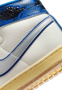 Hvid og blå højt opsnøret sneaker med struktureret blåt ankelkrave, grå sidestribe og beige struktureret sål, set tæt på.