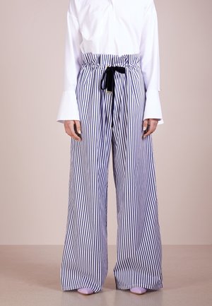 Persoon draagt blauw-witte, verticaal gestreepte broek met hoge taille en wijde pijpen, voorzien van een zwarte strikriem, witte blouse en lavendelkleurige puntige schoenen.
