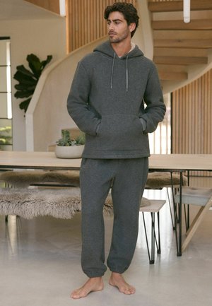 Felpa grigia con cappuccio e pantaloni coordinati in tessuto morbido, dotati di cappuccio, cordini e polsini elasticizzati. Design minimalista in una vestibilità rilassata.