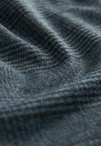 Textured fabric with a dark blue and gray herringbone pattern, slightly shiny surface, and soft, woven appearance, creating gentle folds.