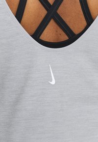 Grå atletisk linne med en vit Nike-logotyp. Har en rundad halsringning och svarta korsryggsremmar för extra stöd.