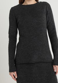 Maglione grigio scuro a maniche lunghe realizzato in un tessuto texturizzato, con scollatura rotonda e bottoni decorativi d'argento sulla spalla.