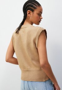 Beezist kudumata särk ilma varrukateta, ribaga alumise servaga ja ümmarguse kaelusega, millel on tekstureeritud kangas ja lahtine lõige, kombineeritud heledate teksadega.