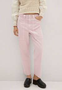 Pantalones sueltos de color rosa claro, con bolsillos laterales y un diseño de pierna ligeramente ancha. Llevados con zuecos negros. Top de punto texturizado.