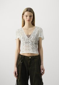 Weißes, kurzes Strickoberteil mit geometrischem Durchbruchsdesign und V-Ausschnitt. Kurze Ärmel mit gestuftem Aussehen.