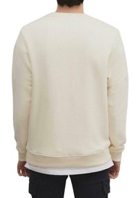 Sudadera color crema con cuello redondo y mangas largas. Presenta una textura suave y puños y dobladillo acanalados.