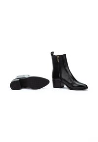 Botas de cuero negras hasta el tobillo con punta afilada, cremallera lateral y tacón cuadrado. La suela presenta un patrón texturizado para mayor agarre.