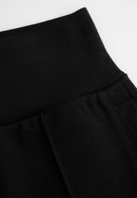 Czarne dresy mają elastyczny, ribbowany pas oraz miękką tkaninę. Projekt zawiera boczne kieszenie oraz gładką fakturę.