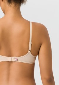 Beiger BH mit schmalen verstellbaren Trägern, Haken- und Ösenverschluss im Rücken, glatter Textur und kleinem Logo-Highlight in der Nähe des Verschlusses.