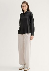 Black long-sleeve shirt with buttons and collar, paired with light beige wide-leg pants and white sneakers with tan soles.
