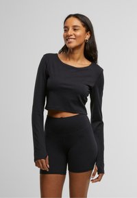 Must mustriga musträni pika varrukas topp, millel on lai kaelus, koos sobivate kõrge taljega lühikesed püksid, mõlemad valmistatud siledast venivast kangast.