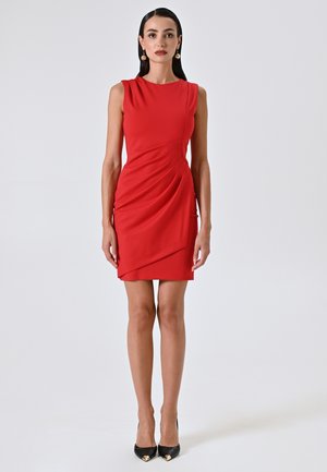 Rotes ärmelloses Kleid mit drapierten Details, taillierter Silhouette, knielangem Saum und glatter Textur. Getragen mit schwarzen High Heels.