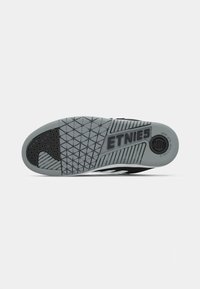 Crna i siva Etnies skate cipela s potplatom koji ima teksturirani uzorak te kružni logo i ojačani nožni dio. Posebno se ističe svojim dizajnom za prianjanje.