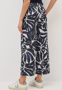 Wijduitlopende broek in marineblauw met een witte bloemenprint, voorzien van een elastische tailleband, een soepele katoenen stof en zijzakken. Draagt samen met witte sneakers.