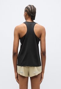 Czarny top na ramiączkach w stylu racerback, lekki materiał, dopasowany krój, z kontrastowymi przeszyciami. Połączony z beżowymi szortami z odblaskowymi detalami.