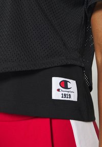 Black mesh sports jersey featuring a Champion brand tag with a logo and "1919" in red and black. Soft fabric with a breathable texture.