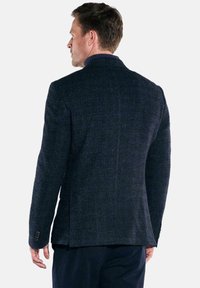 Dunkelblazer mit Struktur und subtilen Mustern, mit einer einfachen Belüftung auf dem Rücken und geknöpften Bündchen. Der Stoff hat einen leichten Glanz.