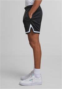 Shorts de sport noirs avec des accents blancs et des fentes sur les côtés, fabriqués dans un tissu léger. Stylisés avec un t-shirt blanc assorti et des baskets.