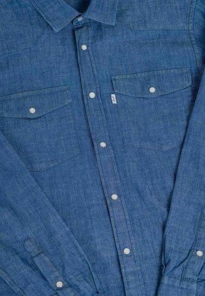 Denim shirt in medium blue with button-up front, two chest pockets, silver snap buttons, and short, rolled-up sleeves.