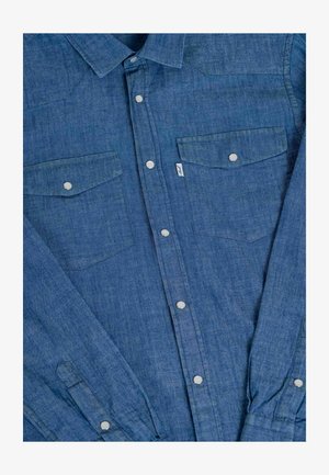 Denim shirt in medium blue with button-up front, two chest pockets, silver snap buttons, and short, rolled-up sleeves.